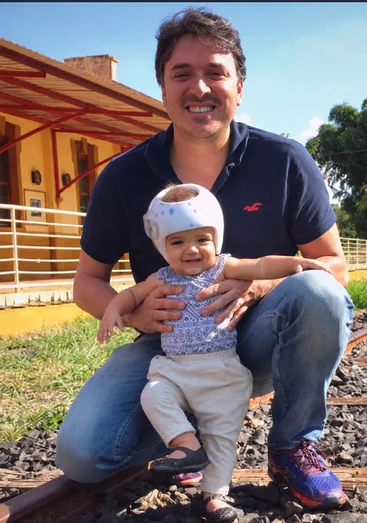 Dr. Jonathan Campos com a filha, bebê usando órtese craniana